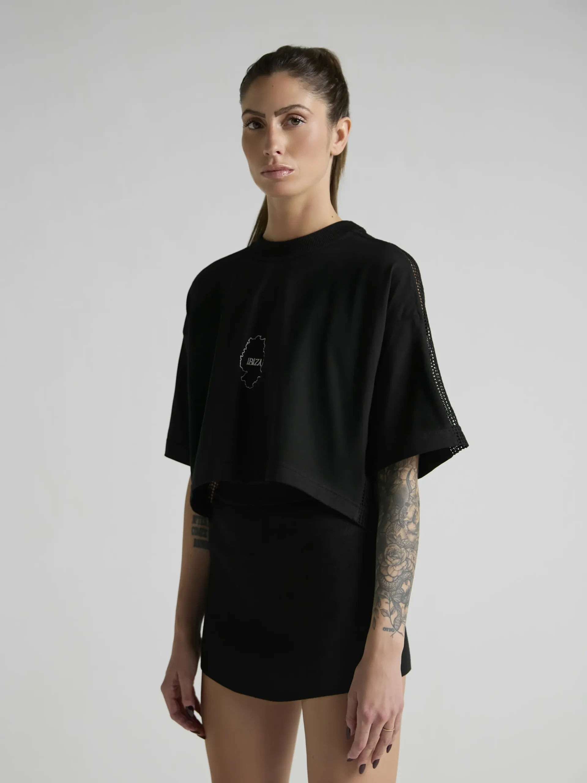 Women's black crop top with mesh inserts on shoulders and sides by UNRULED IBIZA collection.