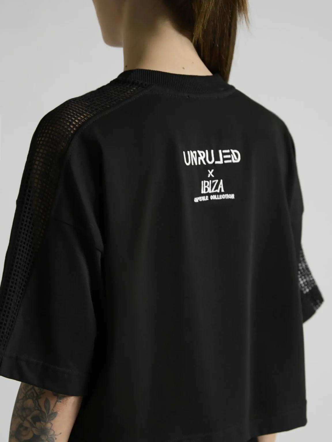 Women's black crop top with mesh inserts on shoulders and sides by UNRULED IBIZA collection.