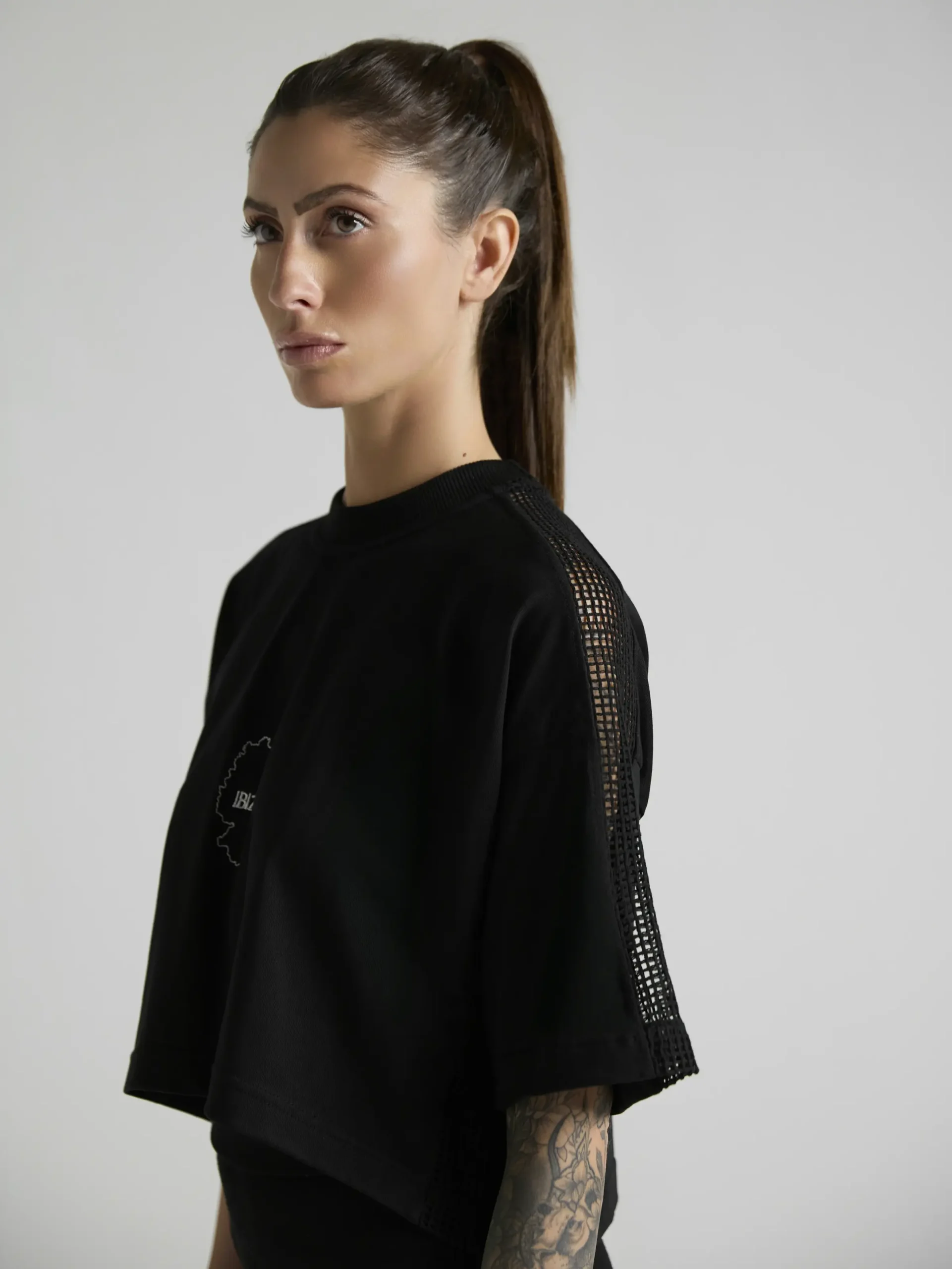 Women's black crop top with mesh inserts on shoulders and sides by UNRULED IBIZA collection.
