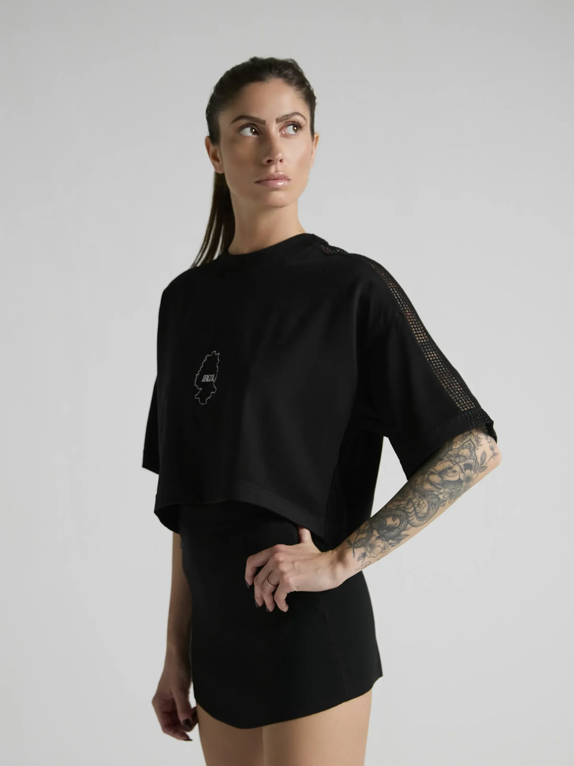 Women's black crop top with mesh inserts on shoulders and sides by UNRULED IBIZA collection.