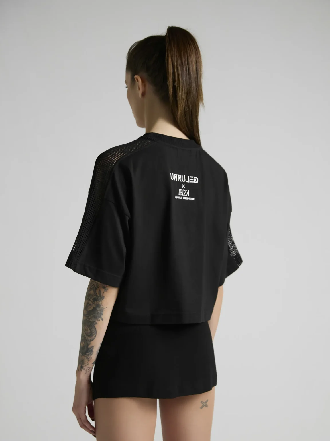 Women's black crop top with mesh inserts on shoulders and sides by UNRULED IBIZA collection.